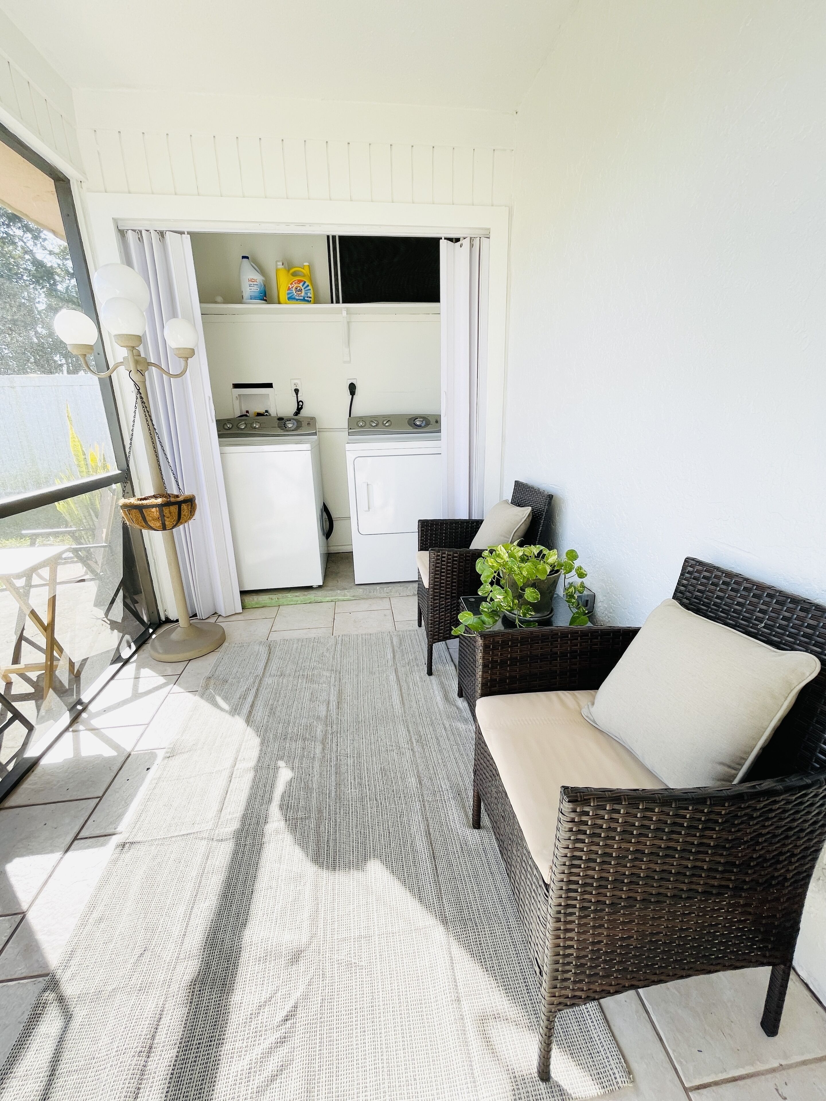 A bright, sunlit room with a wicker sofa, a small table, and a view of a kitchen through a doorway.