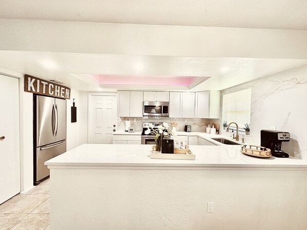 A modern kitchen with white cabinetry, stainless steel appliances, and a central island. - Modern boho 2bed 2bath home, 8 mins to downtown cape and near beach. (Cape Coral)