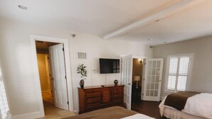 Un dormitorio con una cama grande, un aparador, un televisor y una puerta que da a otra habitación.