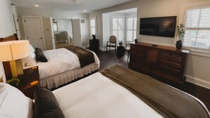 A hotel room with two beds, a TV, a desk, and a chair. - Southern Pines • The Jefferson Inn • Deluxe 2-Queen Guestroom (Southern Pines)