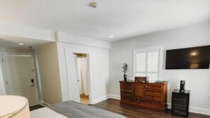 A bedroom with a bed, dresser, TV, and a door leading to another room. - The Jefferson Inn, Downtown Southern Pines, King Bed (Southern Pines)