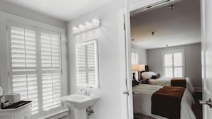 A bedroom with a bed, a bedside table, and a window. - Southern Pines • The Jefferson Inn • Deluxe 2-Queen Guestroom (Southern Pines)