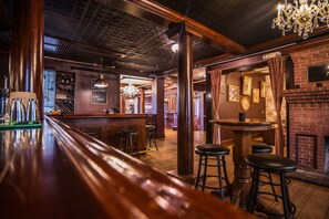 A bar area with wooden bar stools, a brick fireplace, and a chandelier.