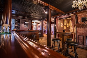 A bar area with wooden bar stools, a brick fireplace, and a chandelier. - Southern Pines • The Jefferson Inn • Standard 2-Queen Room (Southern Pines)
