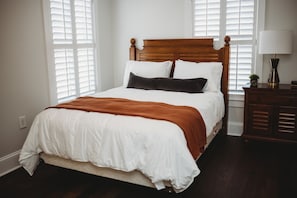 A neatly made bed with a wooden headboard, white bedding, and a brown throw blanket. - Southern Pines • The Jefferson Inn • Standard 2-Queen Room (Southern Pines)