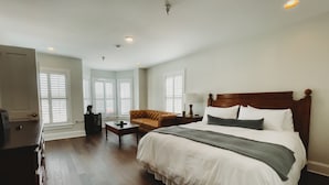 Une chambre spacieuse avec un grand lit, une tête de lit en bois, une table de chevet, une commode, un canapé et un téléviseur.