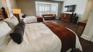 A hotel room with two beds, a sofa, a TV, and a dresser. - Southern Pines • The Jefferson Inn • Deluxe 2-Queen Guestroom (Southern Pines)