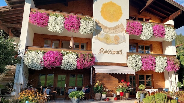 Un hotel con balcones decorados con flores, fachada de madera y un letrero que dice 'Kaisermühle'.