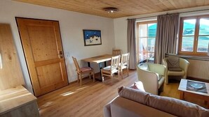 Una sala de estar acogedora con piso de madera, un sofá, una mesa de comedor con sillas, un televisor y una ventana con cortinas.