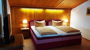 Una habitación con paneles de madera, una cama, dos lámparas de noche, una silla y un cuadro en la pared.