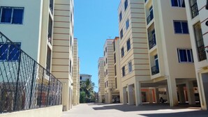Un immeuble résidentiel à plusieurs étages, doté de balcons, d’une entrée sécurisée et surplombant un ciel dégagé.
