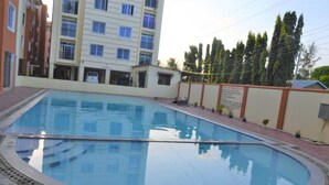 Une piscine dont le bord est recouvert de carreaux, entourée d’un chemin pavé en briques et d’un petit muret sur lequel est apposée une pancarte.