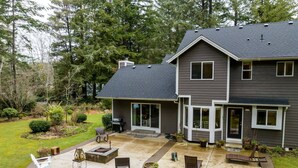 A two-story house with a covered patio area featuring outdoor seating and a fire pit. - New Listing! Beautiful well appointed Woahink lake area home w/ gas grill and fire pit (Florence)