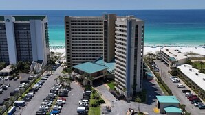 A high-rise hotel with multiple floors, a parking lot, and a beach view.