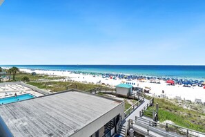 A beach view with a pool, beach umbrellas, and a clear sky.
