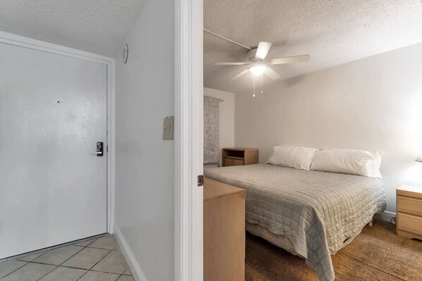 A bedroom with a bed, a nightstand, a wooden dresser, a ceiling fan, and a door.