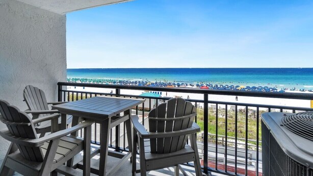 A balcony with a view of a beach, a table, and two chairs.