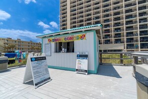 Un quiosco en la playa con un cartel que dice 'Snow Cones' y un panel de menú para los servicios de playa 'La Dolce Vita'.
