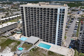 A high-rise hotel with multiple floors, a swimming pool, and a parking lot.