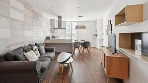 Um espaço de estar moderno com um sofá cinzento, uma mesa de jantar com cadeiras, uma área de cozinha e estantes embutidas.