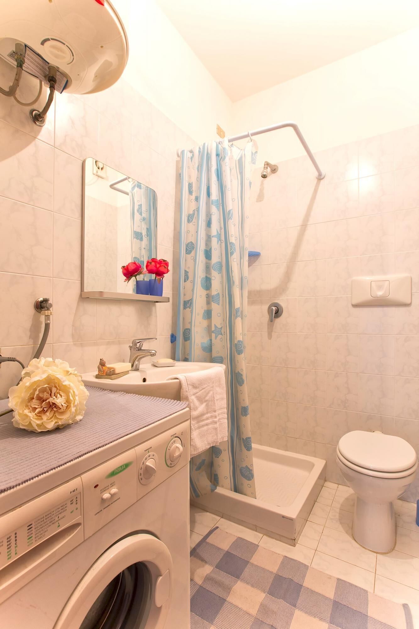 Une salle de bain équipée d’un lave-linge, d’un évier, de toilettes et d’une douche avec un rideau à motifs bleus et blancs.