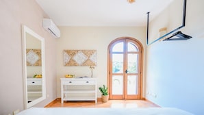 A bedroom with a bed, a dresser, a mirror, a wall-mounted air conditioner, a wooden door, and a hanging light fixture. - Lemon Garden Room Superior (Ravello)