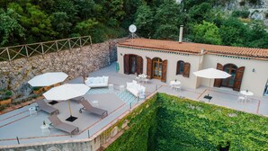 A rooftop terrace with outdoor seating, a stone wall, and a building with wooden doors and windows. - Lemon Garden Room Superior (Ravello)