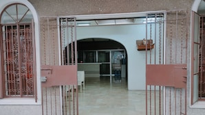 Una entrada con reja a un edificio con suelo de baldosas y un arco de entrada que da a una habitación con escritorio y sillas.