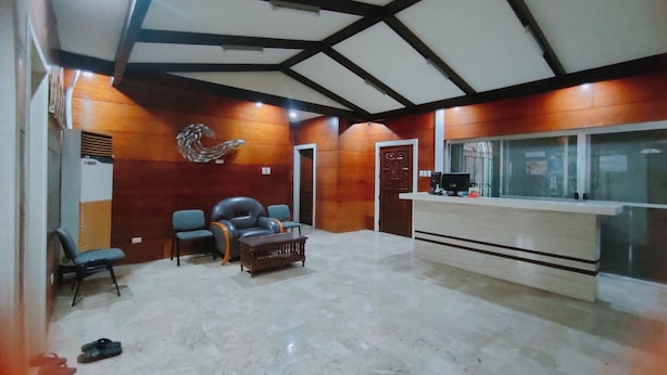 Un área de recepción con un mostrador de madera, un espacio de asiento con una butaca de cuero y un adorno en la pared.
