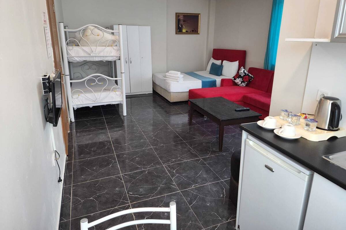 A compact hotel room with a bunk bed, a sofa, a coffee table, and a kitchenette.