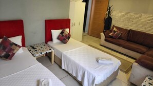 Une chambre d’hôtel avec deux lits simples, un canapé, une petite table et une armoire.