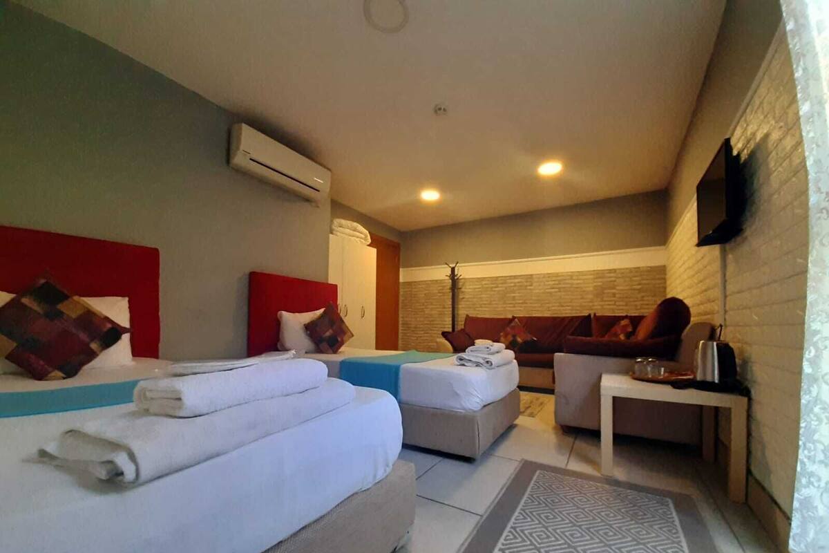 A hotel room with two beds, a sofa, a small table, and a TV mounted on the wall.