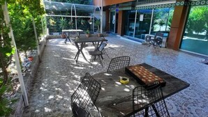 Une terrasse extérieure avec un sol carrelé, des chaises en métal et une table sur laquelle est posé un jeu de société.