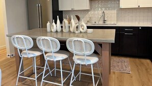 A modern kitchen with white cabinetry, a stainless steel refrigerator, a sink, and a dining area with a table and four white chairs. - Chris's Sweet Suite - 84 Walkscore!! (Seattle)