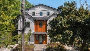 A two-story house with a wooden front door, a small porch, and a garden area with trees and shrubs. - Ringo's Sweet Suite - 84 Walkscore!! (Seattle)