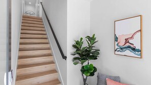 A staircase with wooden steps and a black handrail, a wall-mounted plant, and a framed abstract painting. - Ringo's Sweet Suite - 84 Walkscore!! (Seattle)