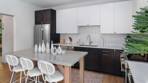 A modern kitchen with white cabinets, a stainless steel refrigerator, and a dining area with a table and chairs. - Ringo's Sweet Suite - 84 Walkscore!! (Seattle)