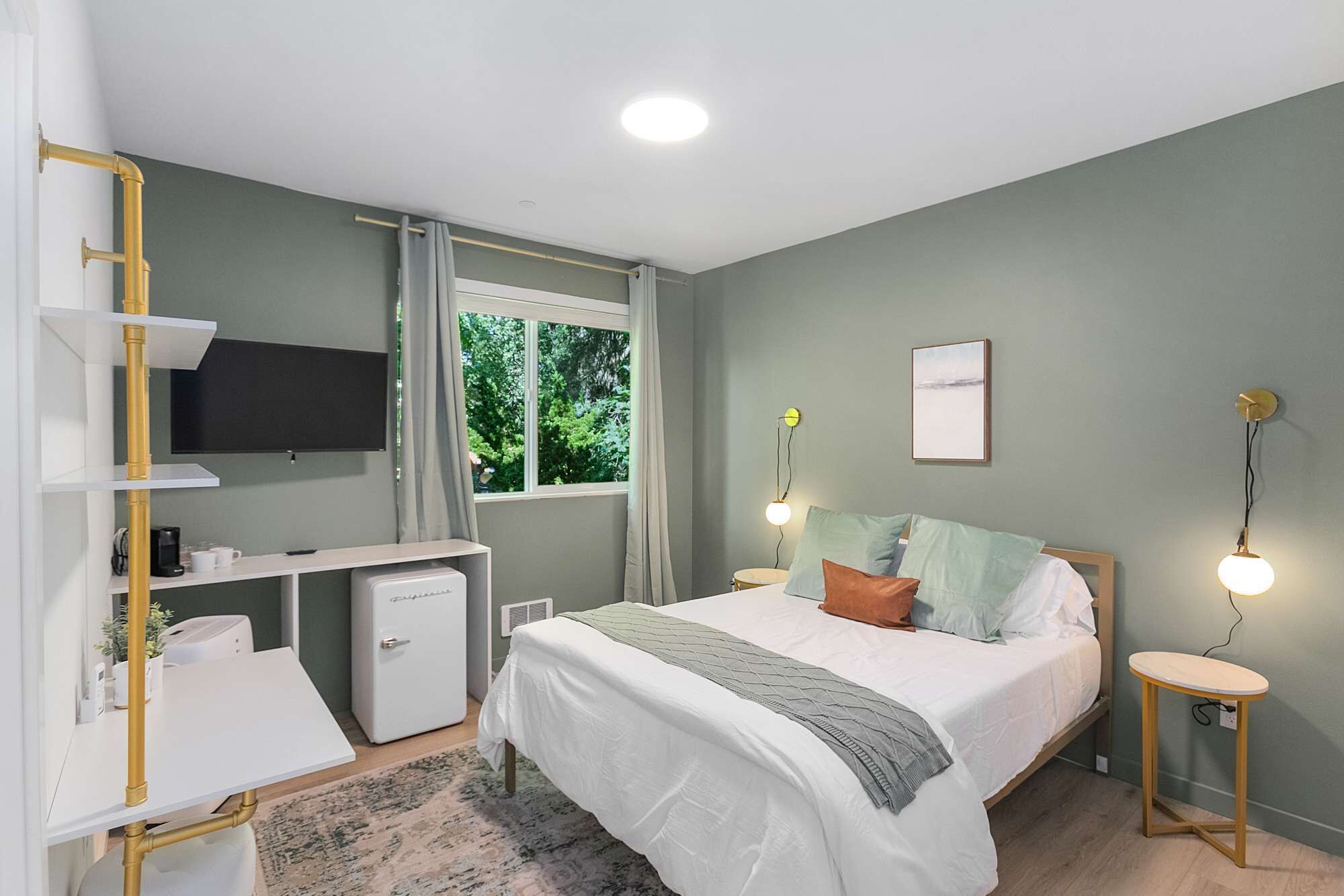 A bedroom with a bed, bedside tables, a TV, a small desk, and a window with curtains.