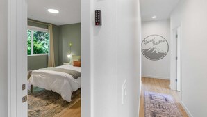 A bedroom with a bed, a nightstand, a wall-mounted lamp, and a door leading to another room. - Kurt's Sweet Suite - 84 Walkscore!! (Seattle)