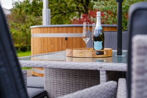 Een glazen tafel met een flesje prosecco en twee glazen op een houten onderzetter.
