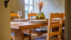 Une table à manger dressée avec des assiettes, des verres et un vase contenant des plumes d’herbe de la pampa.
