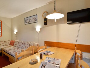 Una stanza accogliente con un tavolo da pranzo in legno, un divano con cuscini decorati, una TV a parete e due applique.