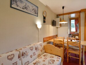 Una stanza accogliente con un divano in legno, un tavolo da pranzo con sedie, una TV a parete e un quadro incorniciato che raffigura montagne.