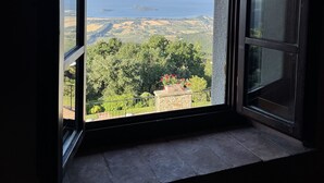 Quarto com uma grande janela que oferece vista para uma paisagem distante, incluindo campos e um corpo d'água.