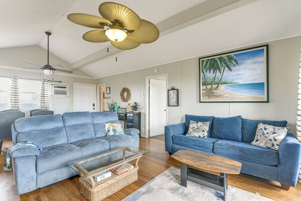 A living room with two blue sofas, a wooden coffee table, a ceiling fan, and a beach-themed painting. - Ocean Views: Second-Row Surfside Beach House (Freeport)