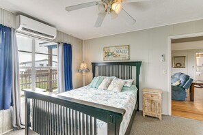A bedroom with a bed, a ceiling fan, a window with curtains, a wall-mounted air conditioner, and a small bedside table. - Ocean Views: Second-Row Surfside Beach House (Freeport)