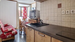 A compact kitchen with wooden cabinets, a black countertop, and a vintage television. - Renovated 2-room apartment, ski-in/ski-out, 4 pers, WiFi (Les Menuires)