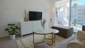 Una sala de estar moderna con un televisor de pantalla plana, una mesa redonda de vidrio, un sofá y una planta en maceta.