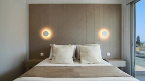 Una habitación de hotel moderna con una cama grande, dos mesitas de noche y vistas a la ciudad a través de un amplio ventanal.