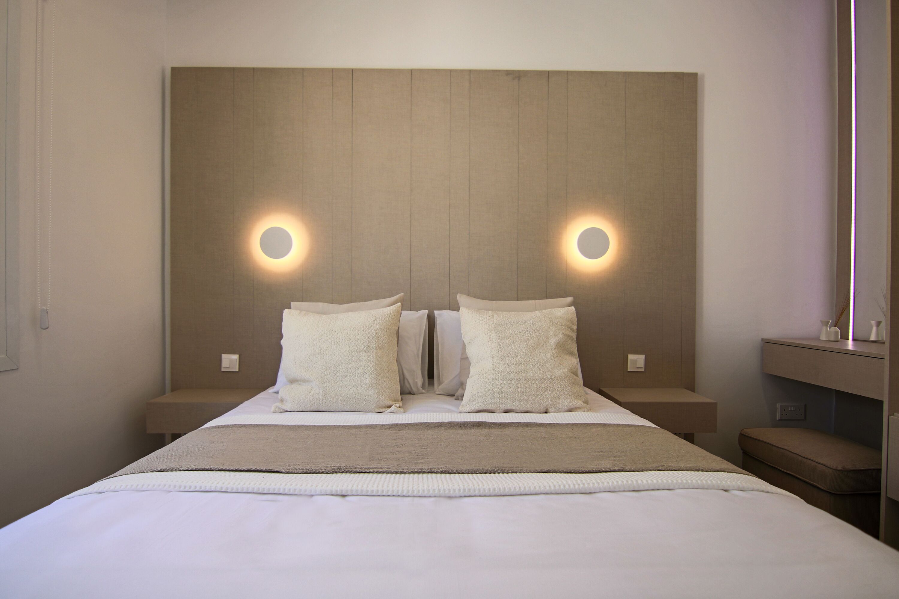 Une chambre d’hôtel moderne dotée d’un grand lit, de deux tables de chevet et d’une tête de lit avec éclairage intégré.